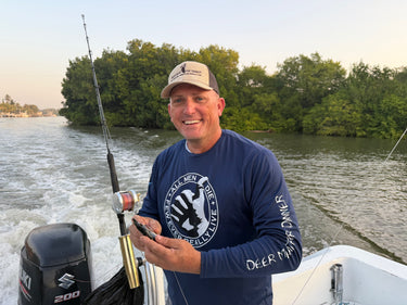 Man on a boat holding a fishing rod with a scenic background wearing the Deer Meat for DInner Team USA shirt